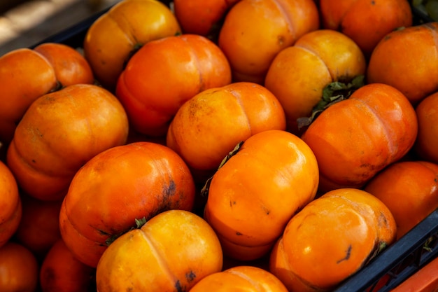 Caqui suculento maduro à luz do sol em uma caixa no mercado. Fechar-se. Vitaminas e saúde da natureza.