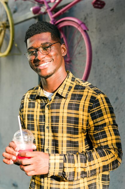 Foto cara afro-americano despreocupado em roupas casuais segurando fundo de verão urbano de coquetel tropical jovem legal bebendo uma deliciosa bebida sem álcool nas férias de verão