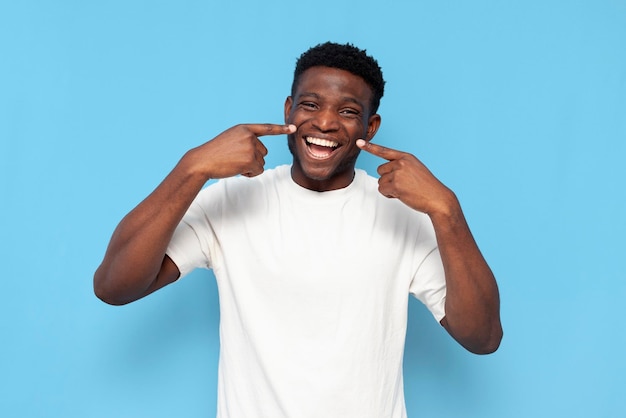 cara afro-americano em camiseta branca sorrindo e aponta para os dentes em fundo azul isolado