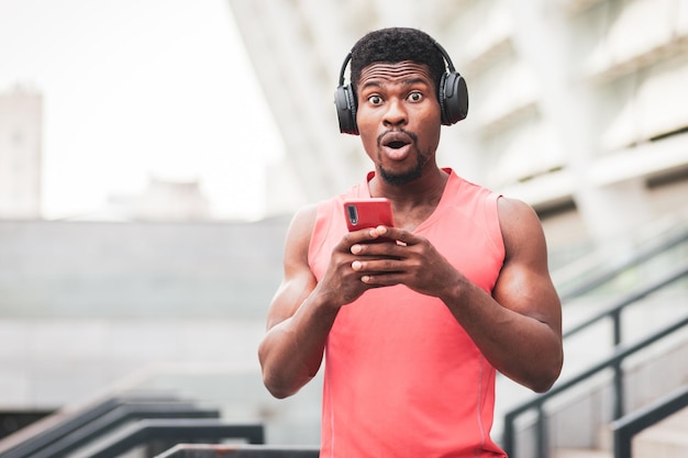 Cara afro-americano surpreso ouvindo música em fones de ouvido contra o fundo