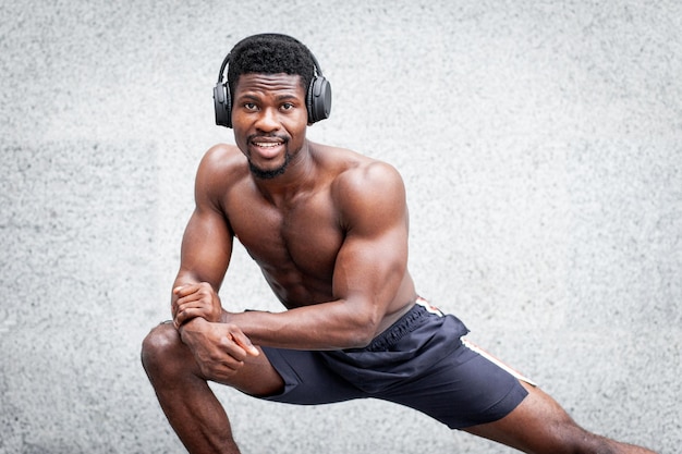 Cara afro-americano treinando ao ar livre contra o homem de fundo de parede com corpo atlético fazendo aquecimento