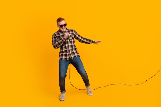 Cara alegre e despreocupado na camisa segurando o microfone cantando karaokê se sentindo feliz aproveitando o fundo amarelo isolado