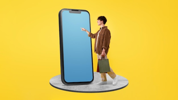 Cara alegre fazendo compras on-line usando celular grande em fundo amarelo