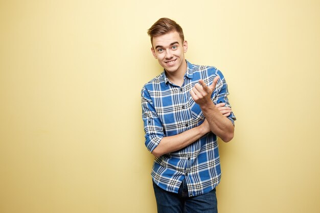 Foto cara alegre, vestida com uma camisa xadrez e jeans fica ao lado da parede amarela no estúdio.