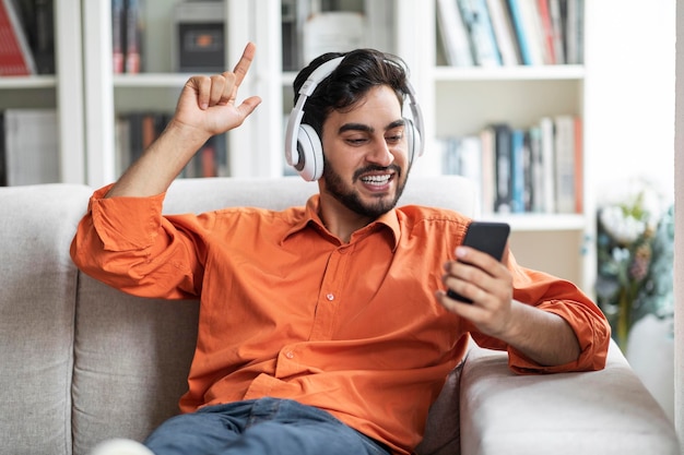 Cara árabe alegre relaxando no sofá em casa ouvindo música