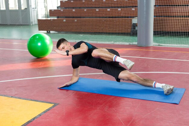 Cara atlético em roupas esportivas e rastreador de fitness, fazendo exercícios no ginásio.