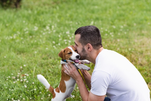Cara atraente abraça e beija seu cachorro Jack Russell Terrier no parque no fundo da grama