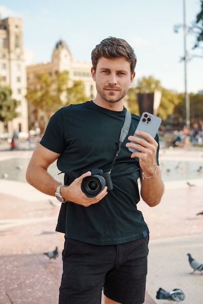 Cara autoconfiante com câmera e smartphone na praça da cidade