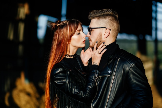 Cara barbudo abraçando com uma garota ruiva ao pôr do sol. Casal apaixonado vestido com jaquetas de couro