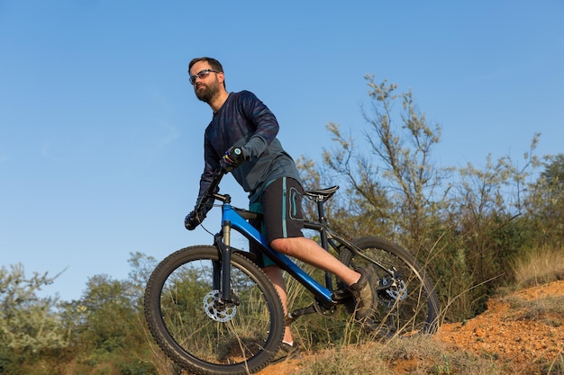 Cara barbudo brutal de esportes em uma bicicleta de montanha moderna Ciclista nas colinas verdes na primavera