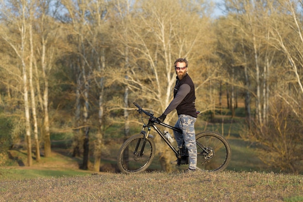 Cara barbudo brutal de esportes em uma bicicleta de montanha moderna ciclista nas colinas verdes na primavera