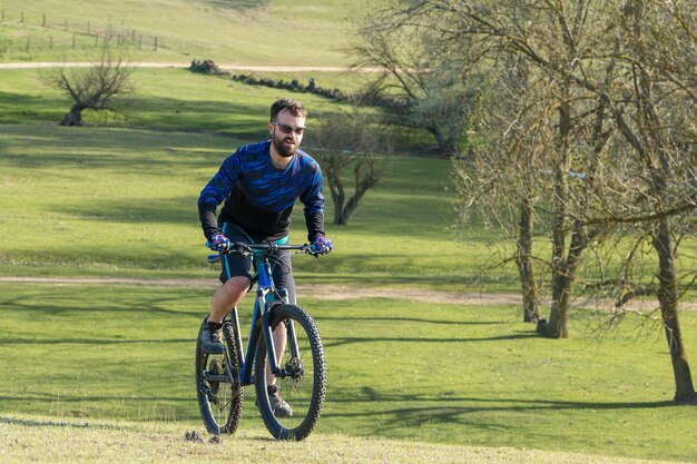 Cara barbudo brutal de esportes em uma bicicleta de montanha moderna Ciclista nas colinas verdes na primavera