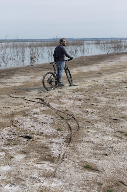 Cara barbudo brutal de esportes em uma bicicleta de montanha moderna Um ciclista em um lugar deserto de sal à beira do lago