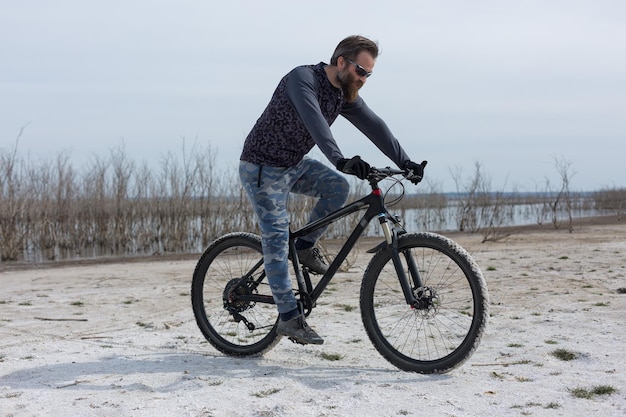 Cara barbudo brutal de esportes em uma bicicleta de montanha moderna Um ciclista em um lugar deserto de sal à beira do lago