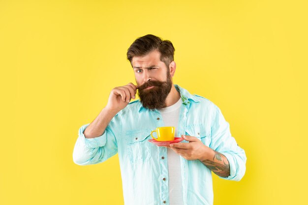 Cara barbudo com bigode bebe café da manhã em fundo amarelo