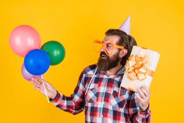 Cara barbudo elegante com penteado moderno usa camisa quadriculada segura balões de festa e aniversário de caixa de presente