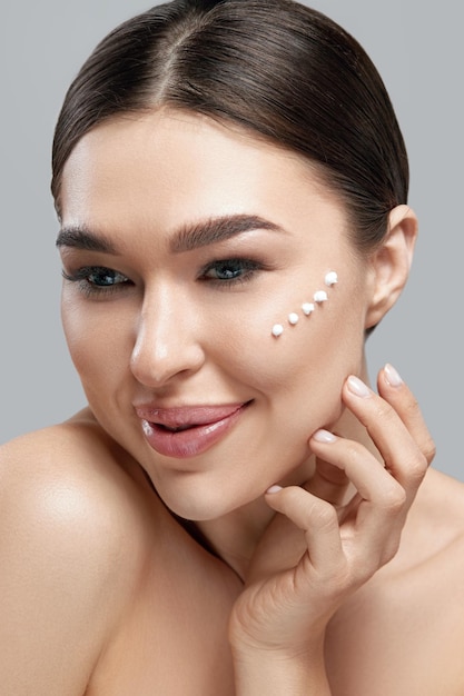 Cara de belleza Mujer hermosa con maquillaje natural Aplicar crema en su rostro Primer plano