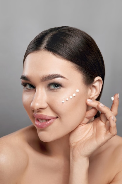 Cara de belleza Mujer hermosa con maquillaje natural Aplicar crema en su rostro Primer plano