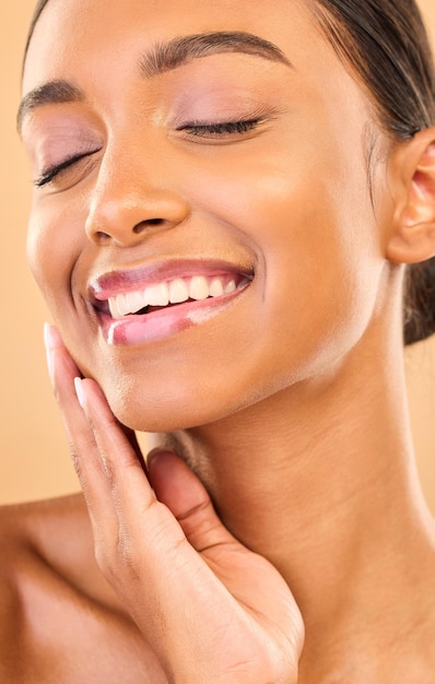 Cara de belleza y sonrisa de mujer con maquillaje en estudio para cosméticos y dermatología para el cuidado de la piel Mano femenina estética para el cuidado personal de la piel natural y el brillo facial del spa resulta en un fondo marrón