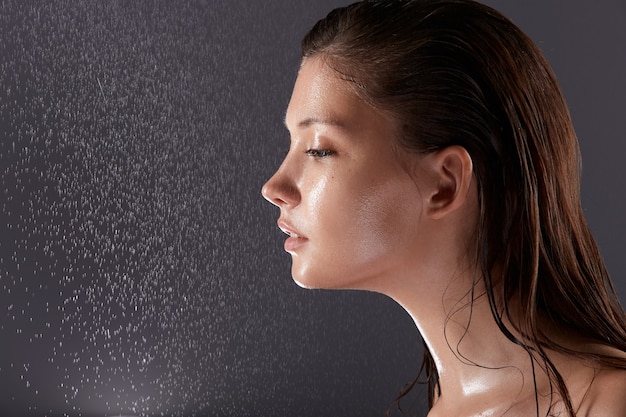 Cara bonita morena de perfil con gotas de agua sobre fondo gris