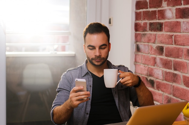 Cara bonito, bebendo café enquanto hodling telefone