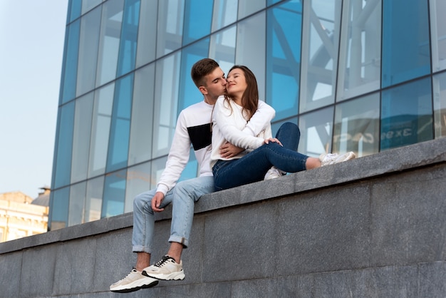 Cara bonito beija a namorada dele. casal apaixonado descansando perto de um edifício moderno. data de um jovem casal na cidade.