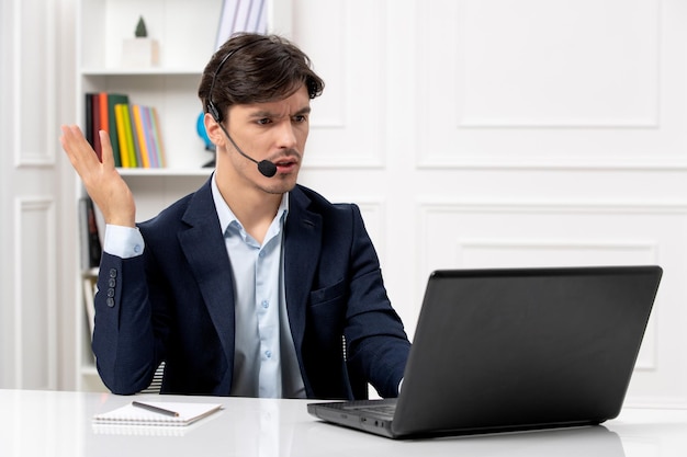 Cara bonito de atendimento ao cliente com fone de ouvido e laptop de terno acenando com as mãos e confuso