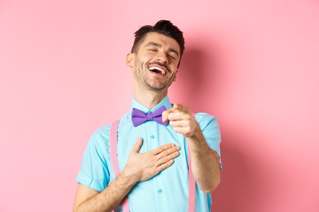 Cara bonito de gravata borboleta apontando o dedo para a câmera e rindo de algo engraçado, conferindo a promoção hilária, de pé na rosa.