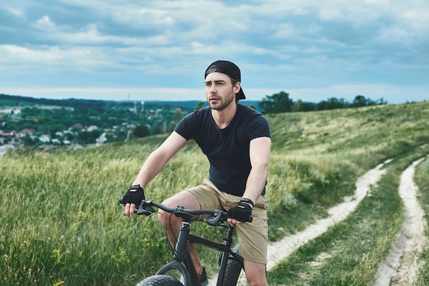 Cara bonito e elegante andando de bicicleta nas montanhas