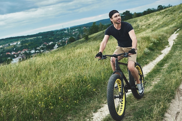 Cara bonito e elegante andando de bicicleta nas montanhas