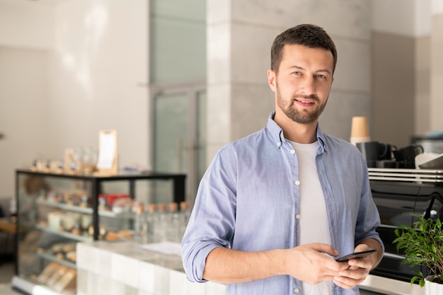 Foto cara bonito em roupas casuais rolando no smartphone enquanto olha para você no café