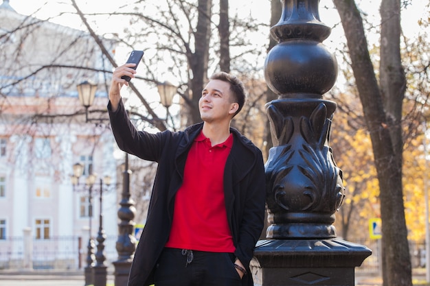 cara bonito em uma caminhada na cidade de outono tira uma selfie