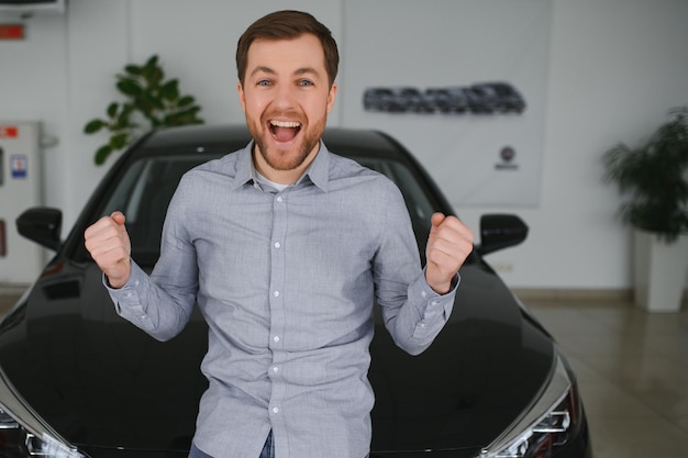 Foto cara bonito emocional levantando a mão e sorrindo para a câmera homem rico comprando carro no salão de concessionária de luxo