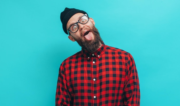 Foto cara bonito hipster com barba sorrindo alegremente vestido casualmente com gorro preto na cabeça isolado sobre um fundo de estúdio azul o conceito de emoções loucas de pessoas