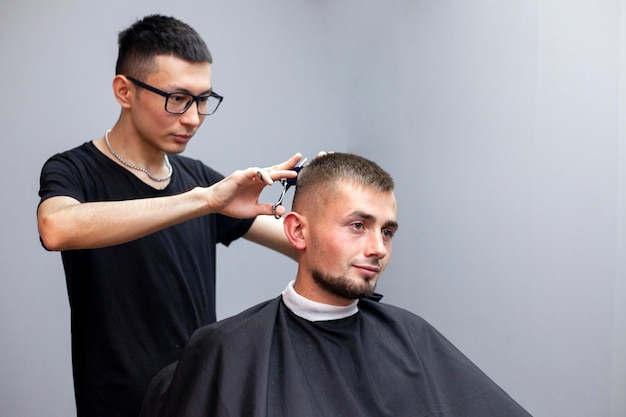 Cara bonito tem um corte de cabelo no cabeleireiro um jovem cabeleireiro cazaque corta manualmente com uma tesoura