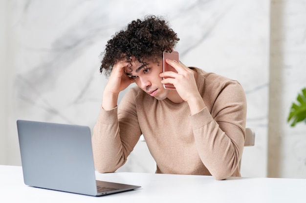 Cara cansado falando no celular e no computador