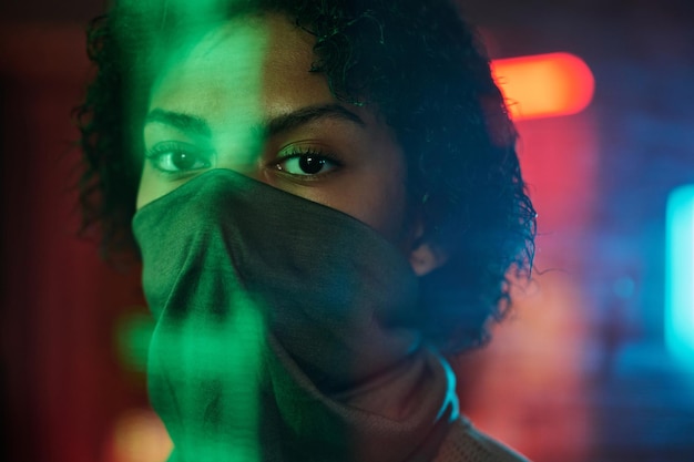 Cara de una chica afroamericana medio cubierta con una máscara parada en un bar cyberpunk