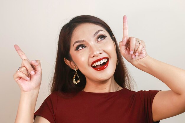 Cara de choque de una joven asiática con una camisa roja apuntando hacia arriba Concepto de publicidad