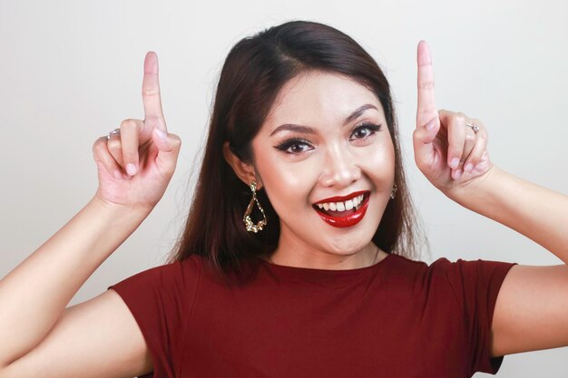 Cara de choque de una joven asiática con una camisa roja apuntando hacia arriba Concepto de publicidad