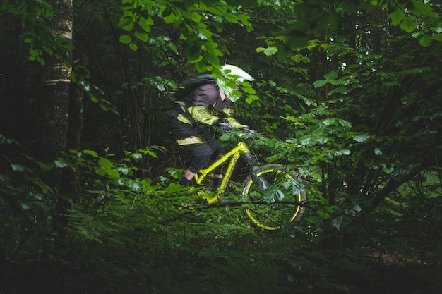 Cara, ciclista no capacete integral anda rápido na bicicleta amarela de enduro na floresta verde