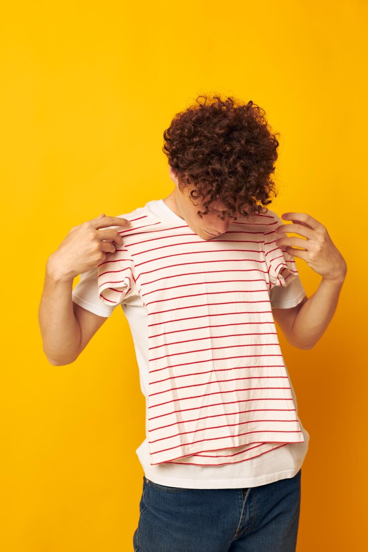 Cara com cabelo encaracolado vermelho em uma camiseta branca segura uma camiseta listrada moda jovem estilo amarelo backgrou