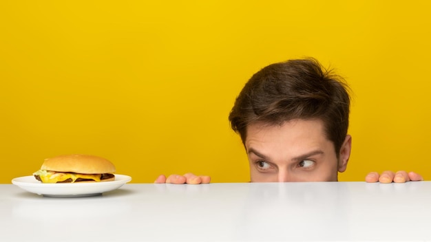 Cara com fome olhando hambúrguer espiando a mesa