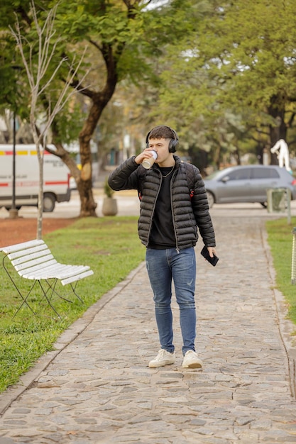 Cara com fones de ouvido bebe café enquanto caminha por um parque público