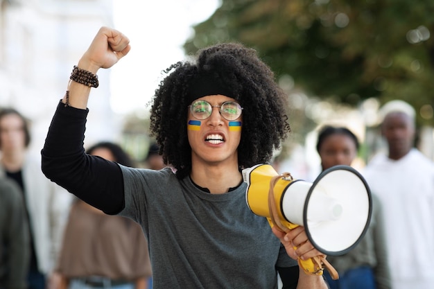 Cara com megafone e rosto pintado liderando grupo de manifestantes