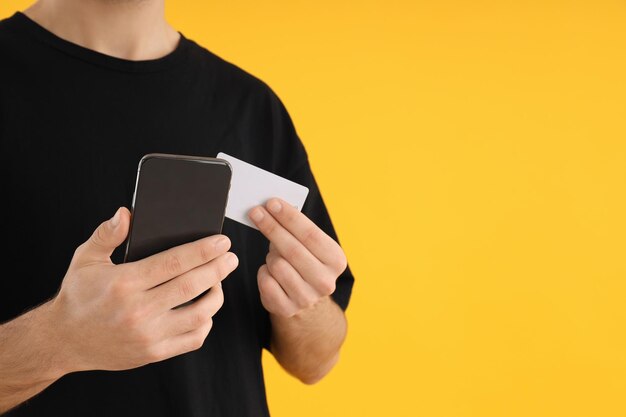 Cara com telefone e cartão de crédito em fundo amarelo