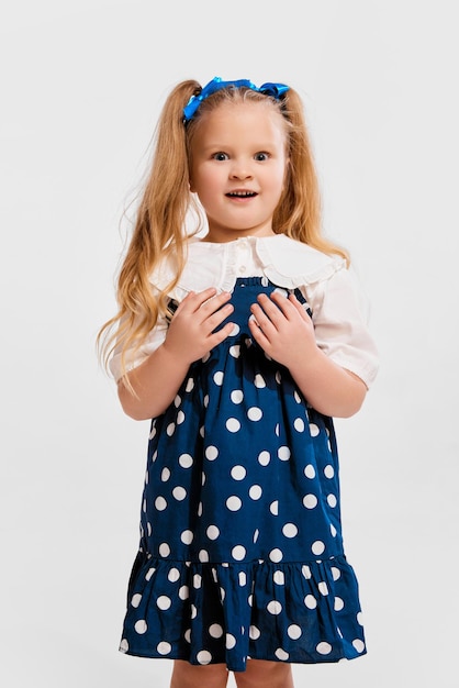 Cara conmocionada Hermosa niña linda con vestido de estilo retro posando sobre fondo gris de estudio Concepto de infancia