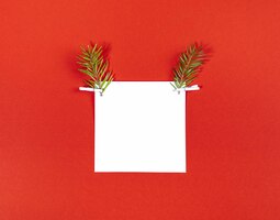 Foto cara creativa de ciervo navideño hecha de hoja cuadrada blanca y dos ramitas de abeto como cuernos de reno en rojo