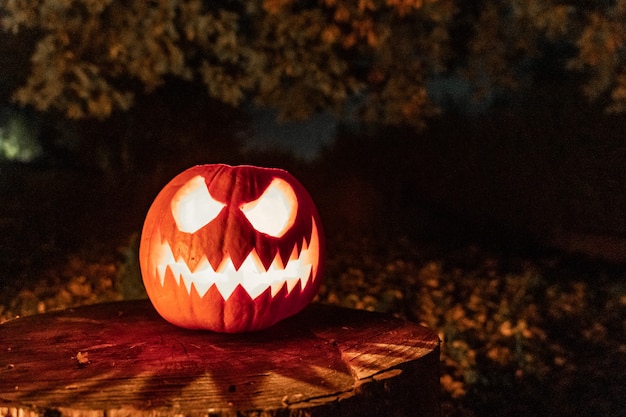 Cara de abóbora de Halloween com vela acesa e acampamento de fogo ao fundo Cara assustadora e fogo de lagoa