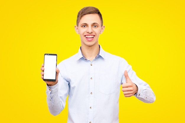 Cara de camisa azul anuncia um telefone isolado em um fundo amarelo no estúdio, mostrando o polegar para cima