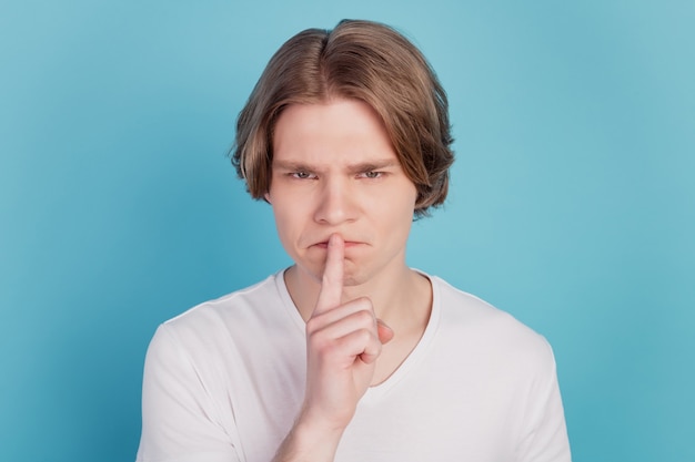 Cara de camiseta branca colocando os lábios dos dedos mostra sinal de silêncio isolado sobre fundo azul